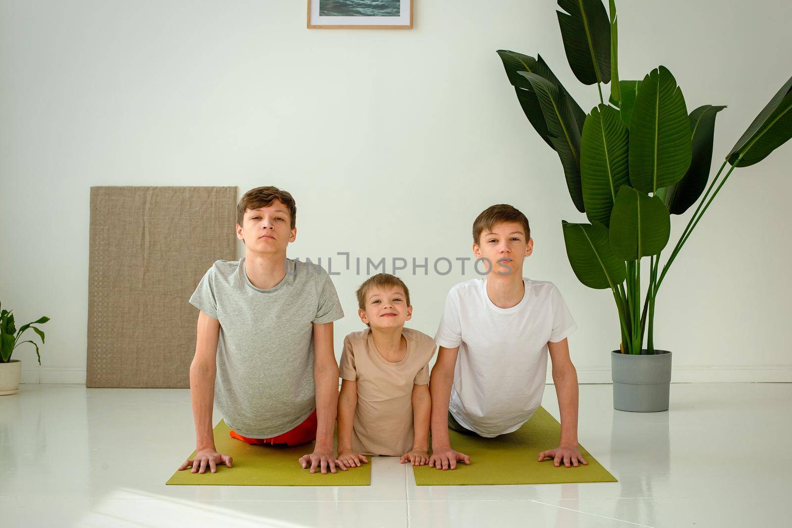 a boy and two teenagers perform a yoga exercise, on mats by Zakharova