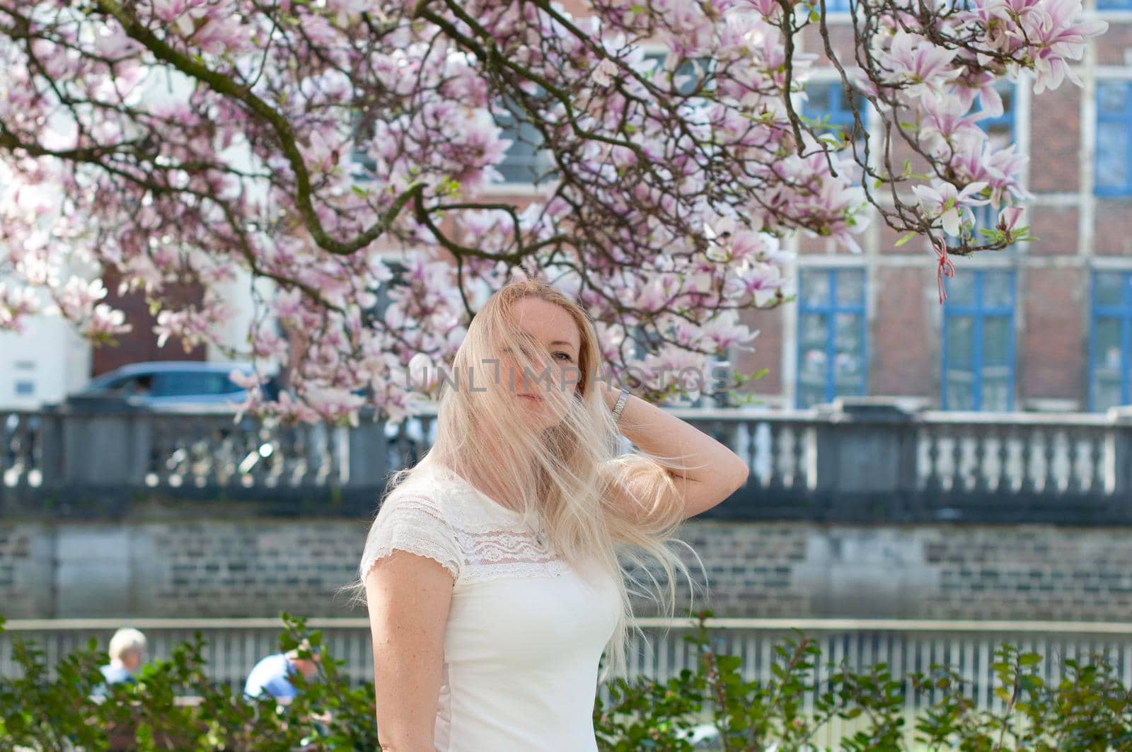 Beautiful young woman with long hair looking at blooming tree with pink magnolia by KaterinaDalemans