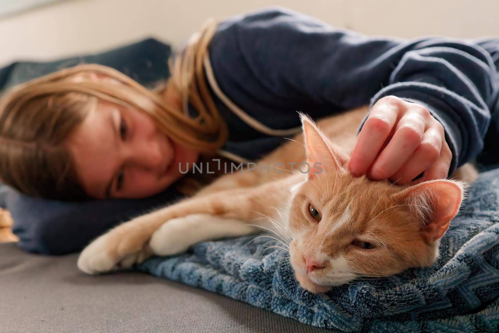 An Young Adolescent girl lying on a couch finds comfort by snuggling close to and petting her tabby cat