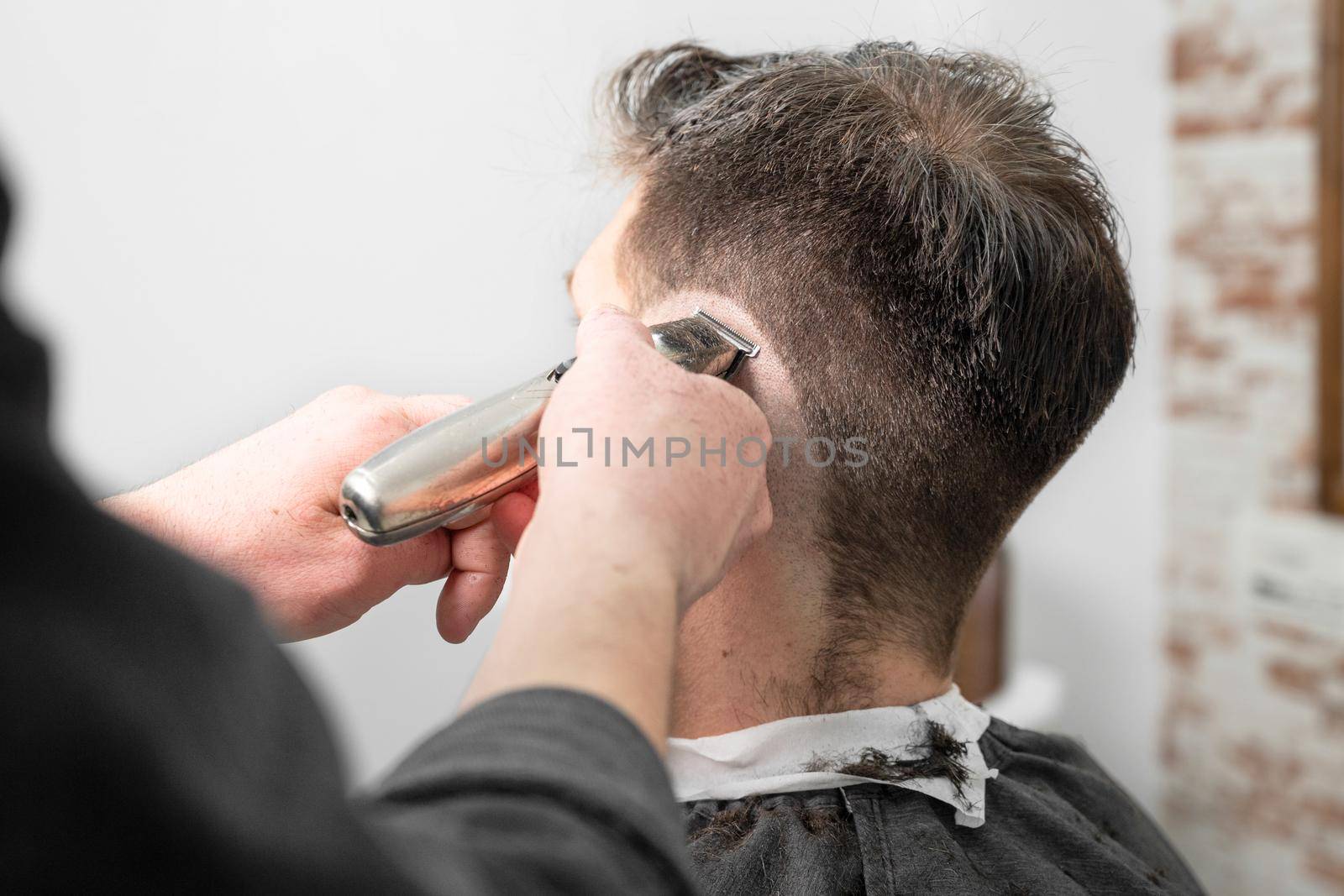 Man barber cutting hair of male client with clipper at barber shop. Hairstyling process. High quality photography