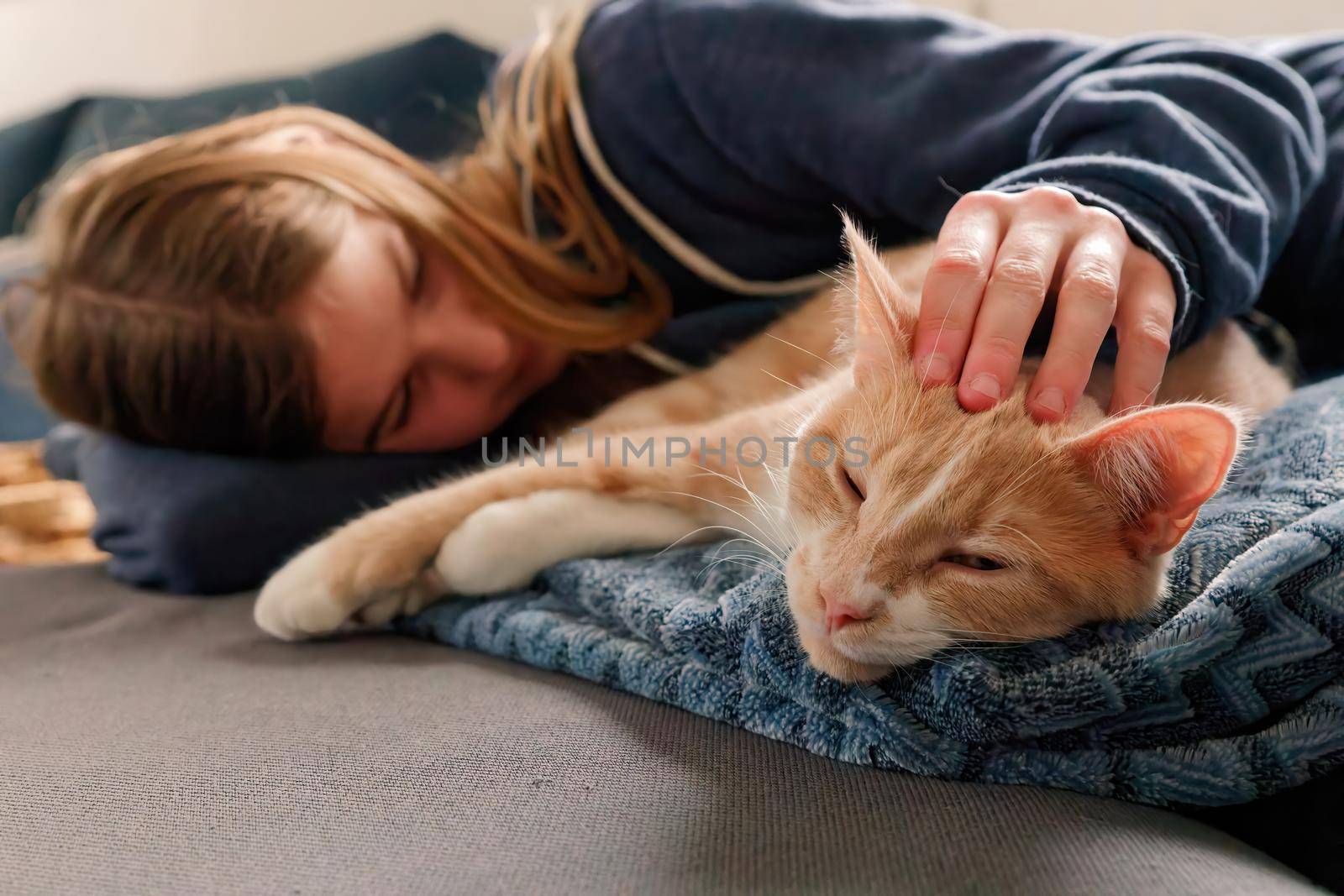 An Young Adolescent girl lying on a couch finds comfort by snuggling close to and petting her cat by markvandam