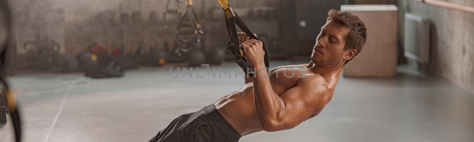 Attractive man intensivly training upper body chest muscles with fitness straps in sport fitness gym club