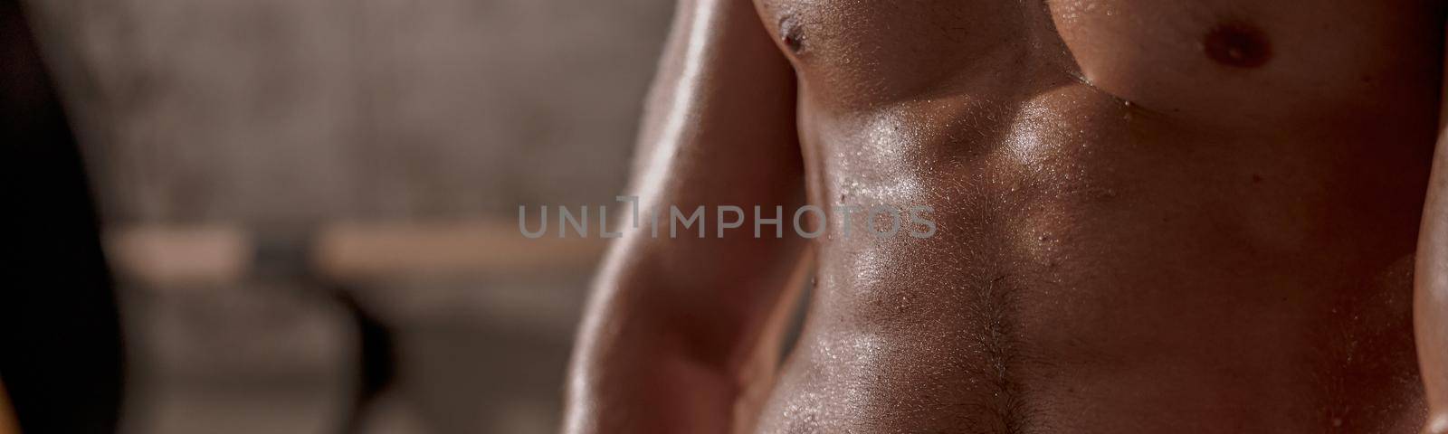 Close up of sporty male with toned torso in drops of sweat on skin at the gym