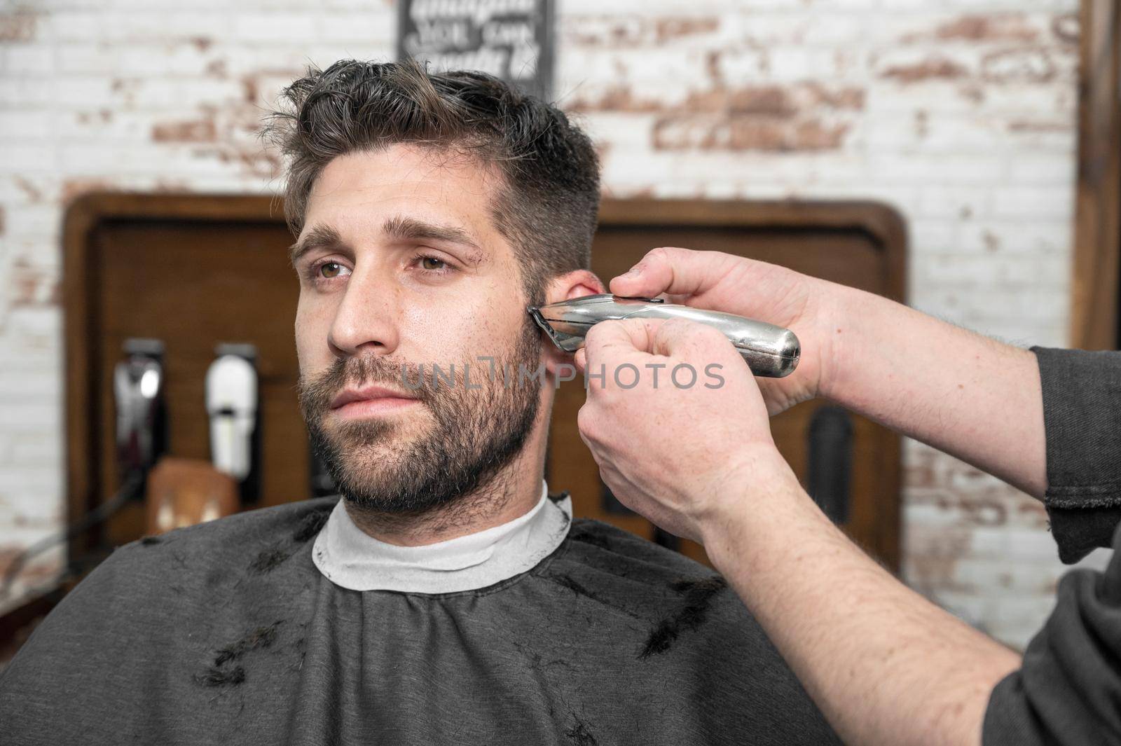 Man barber cutting hair of male client with clipper at barber shop. Hairstyling process. by HERRAEZ