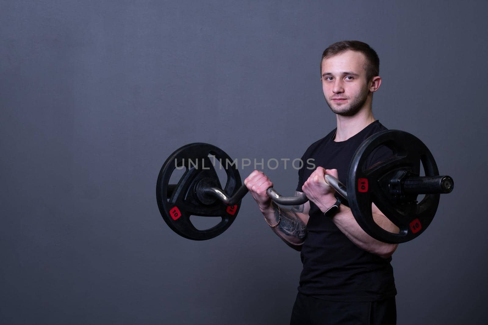 Guy with a barbell in a black fitness T-shirt muscular bodybuilder barbell bodybuilding, from strong active from guy from trainer body, diet triceps. Sportsman young work, practicing arm