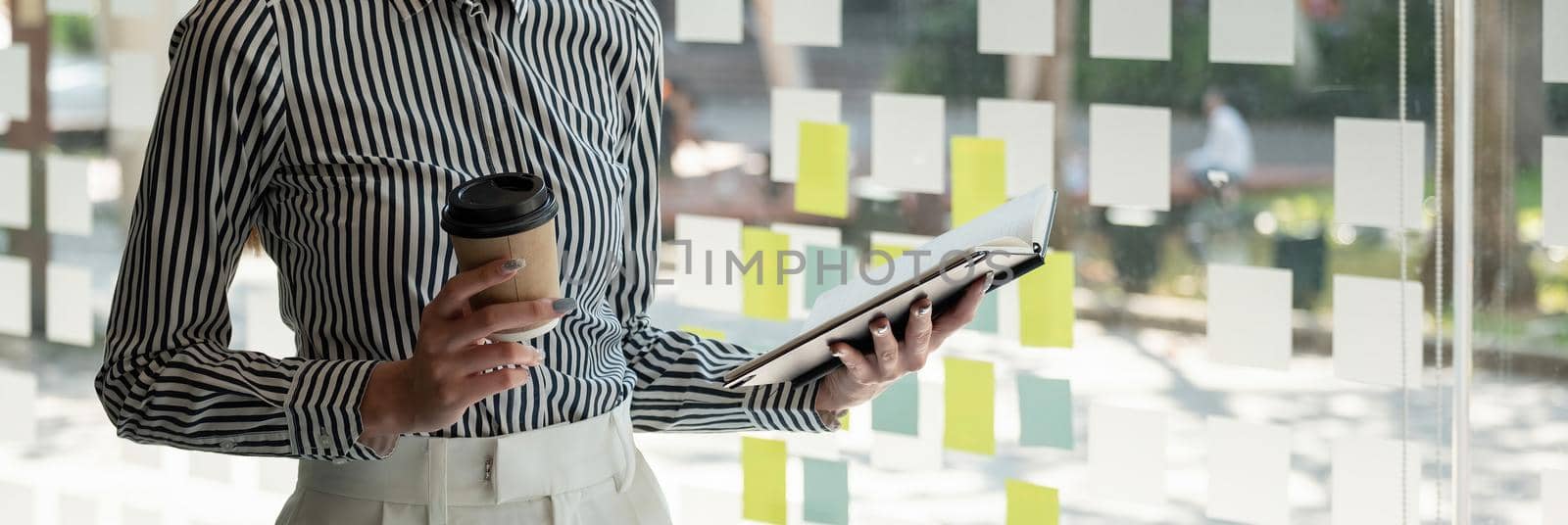 Close up business woman reading a book and writing notes while standing near window