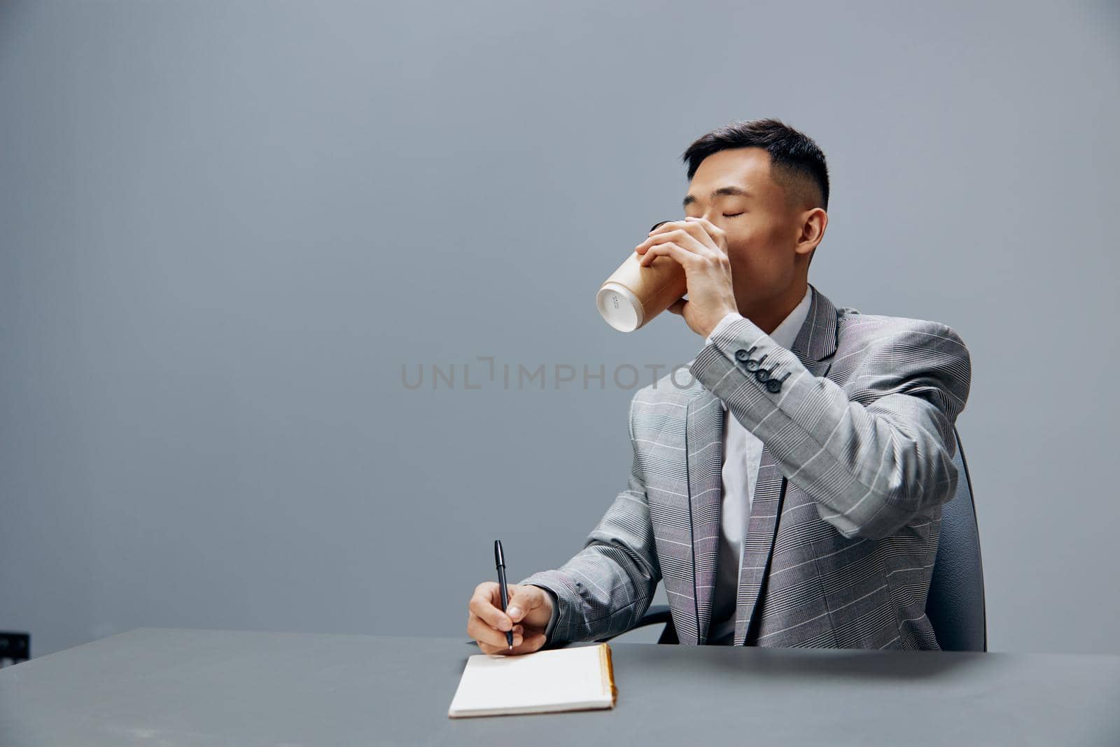 man writes in a notebook sits on the table with coffee official Gray background. High quality photo