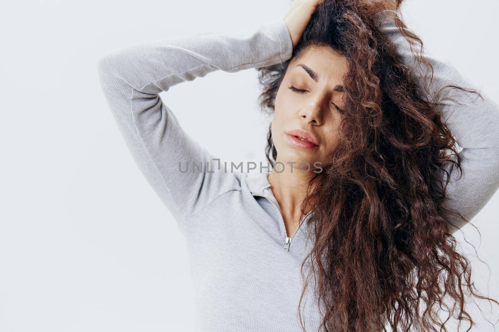 Love Yourself. Close up Shot Curly Latin Female in Pastel Gray Sweater Stroking Hair Closing Eyes, Posing Isolated At White Studio Wall Background. Fashion Seasonal Sale New Collection Concept