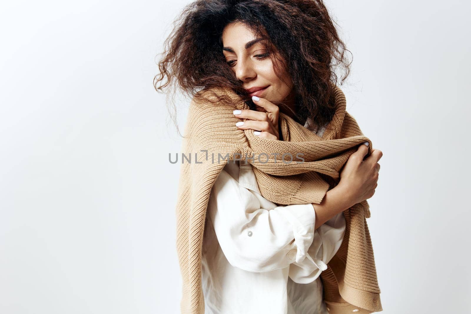 Curly Pretty Latin Female in White Shirt Posing Isolated Hugging Herself Enjoying Warm Sweater Closing Eyes At White Studio Wall Background. Fashion Seasonal Sale New Collection Concept. Copy space