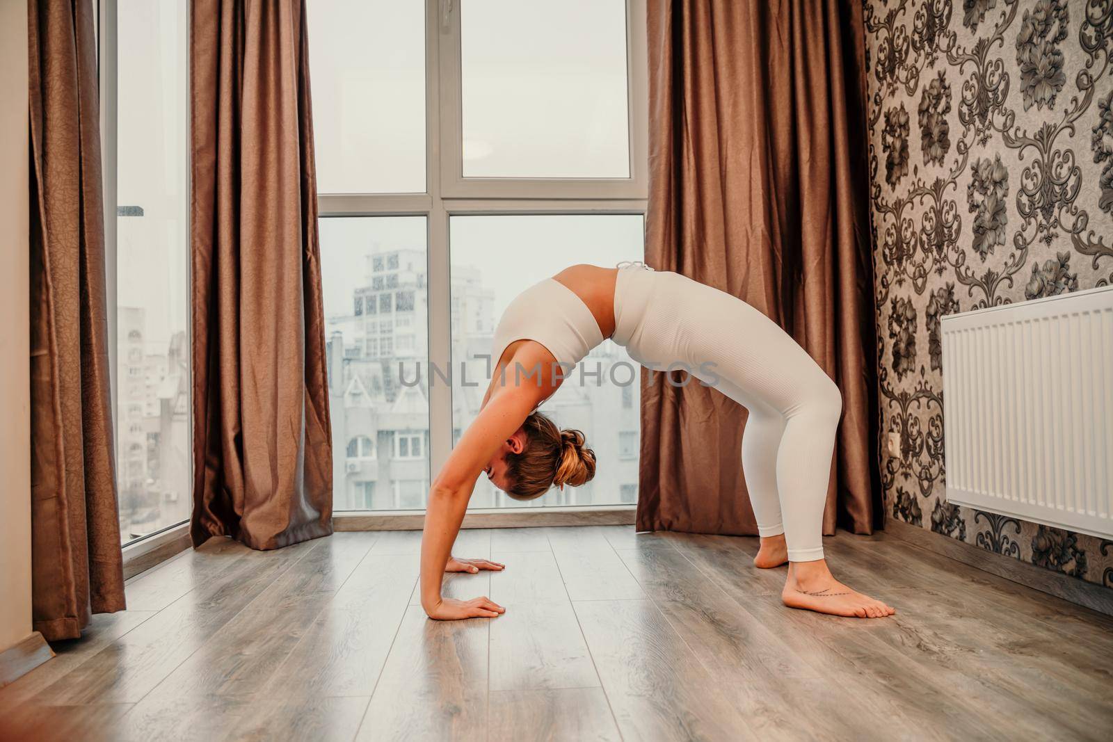 Young athletic attractive woman practicing yoga. Works out at home or in a yoga studio, sportswear, white pants and a full-length top indoors. Healthy lifestyle concept.