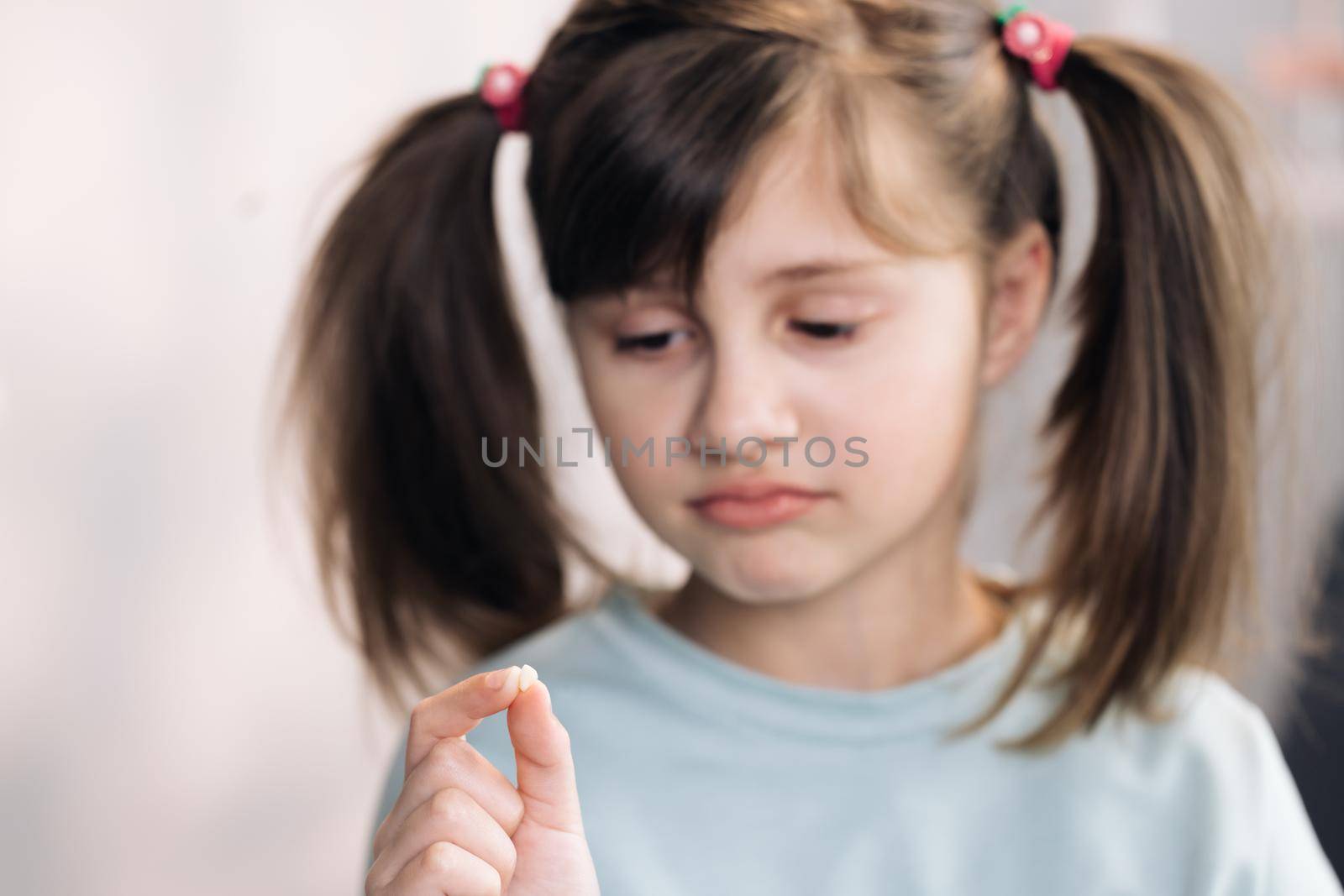 Little girl with milk temporary tooth. Girl holding her fallen tooth in hand. Dental medicine or temporary teeth health care concept.