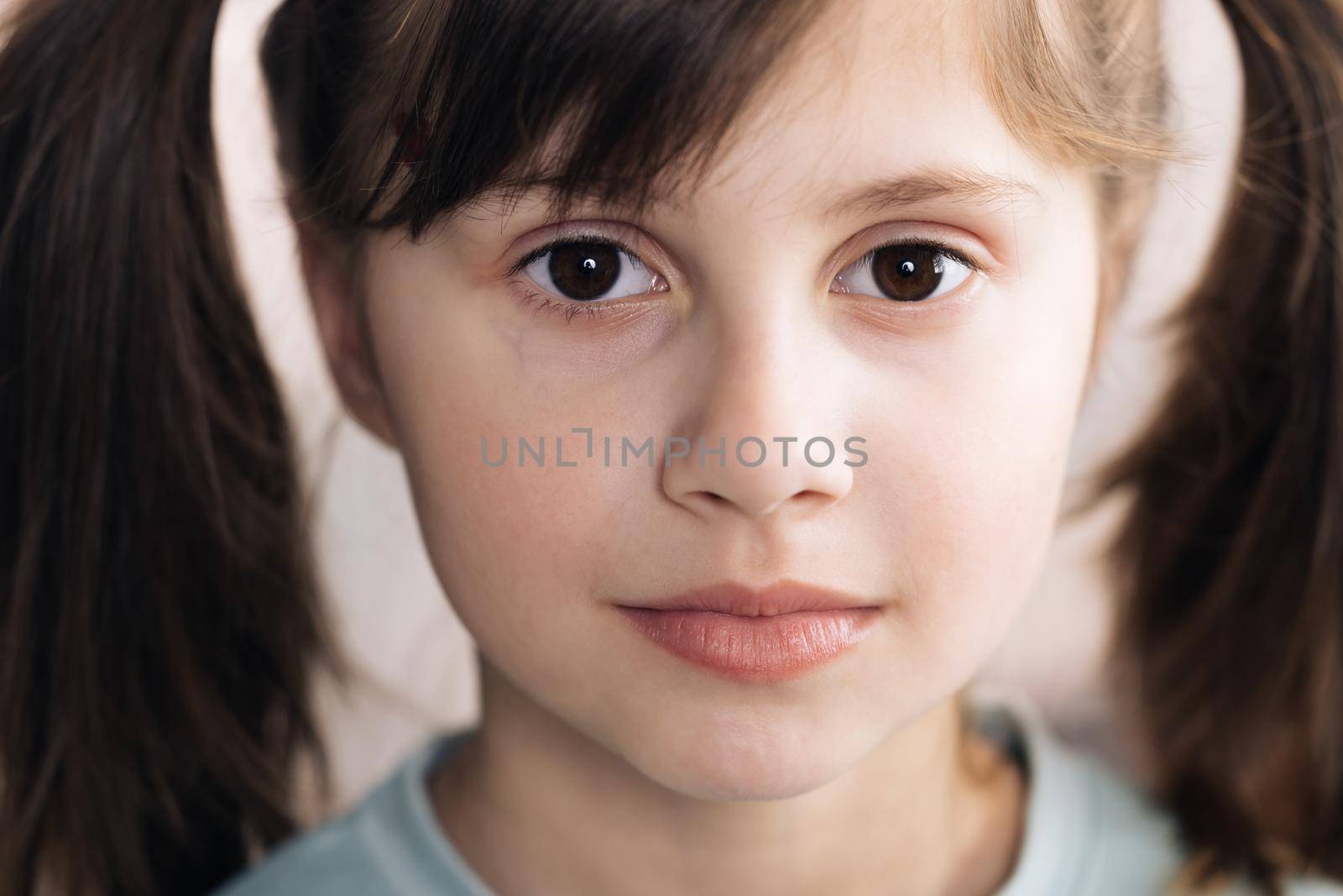 Adorable child with big brown eyes surprisingly react on something, look at camera. Close-up portrait of caucasian black haired girl isolated home. Emotional child