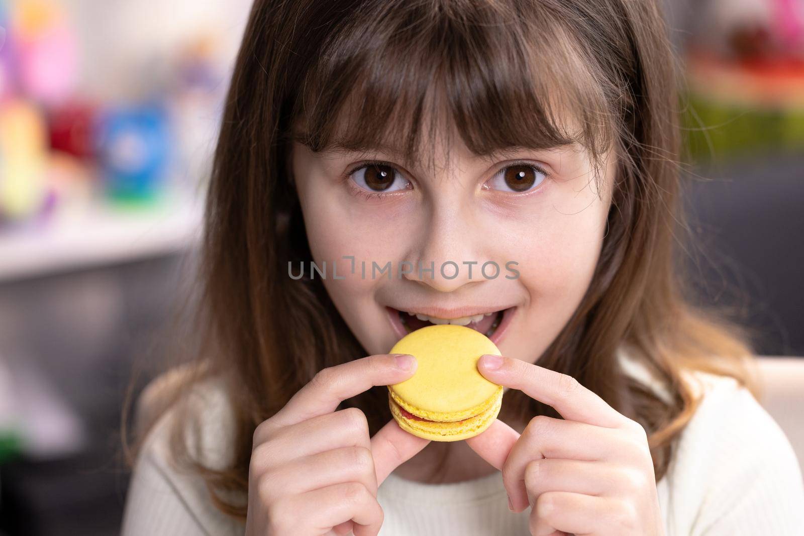 Brunette school girl on a home background, licks her lips, eating one yellow macaron. Dessert person, sweet tooth, gourmet. Feeling good, delicious by uflypro