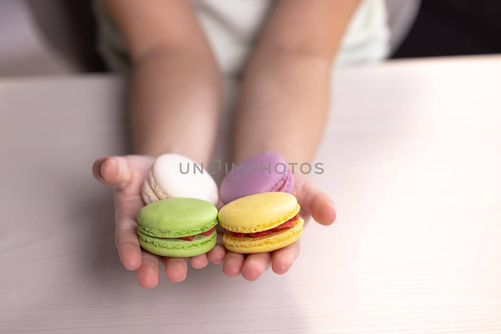 Children's hands hold macarons on a white background. Traditional French multicolored macaroon. Food concept by uflypro