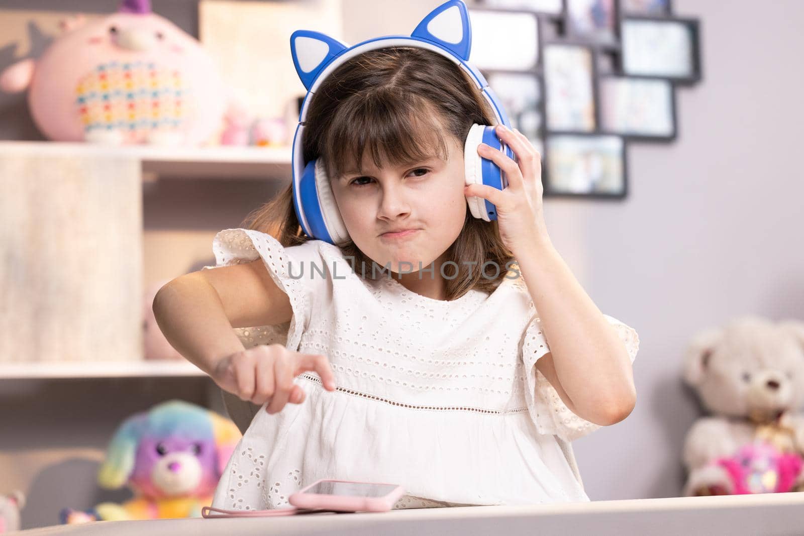 Small kid girl in headphones using funny editing application on smartphone, enjoying cool video or music content in social network, playing online games, communicating distantly.