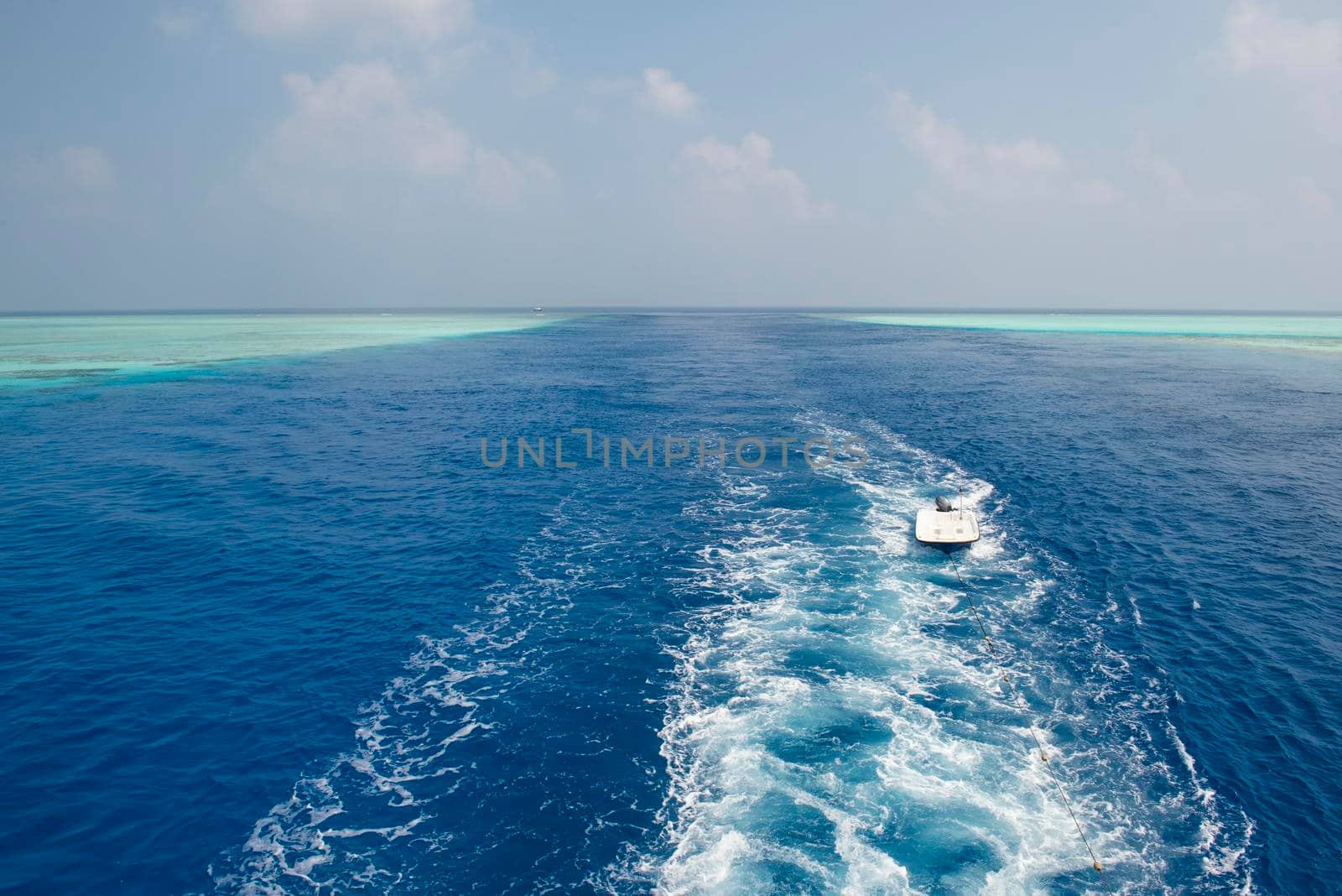Panoramic scenic view of seascape over tropical ocean through channel in coral reef atoll with boat wake