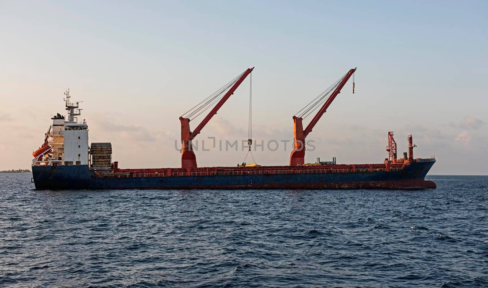 Large cargo container ship at anchor on sea with jib cranes and superstructure