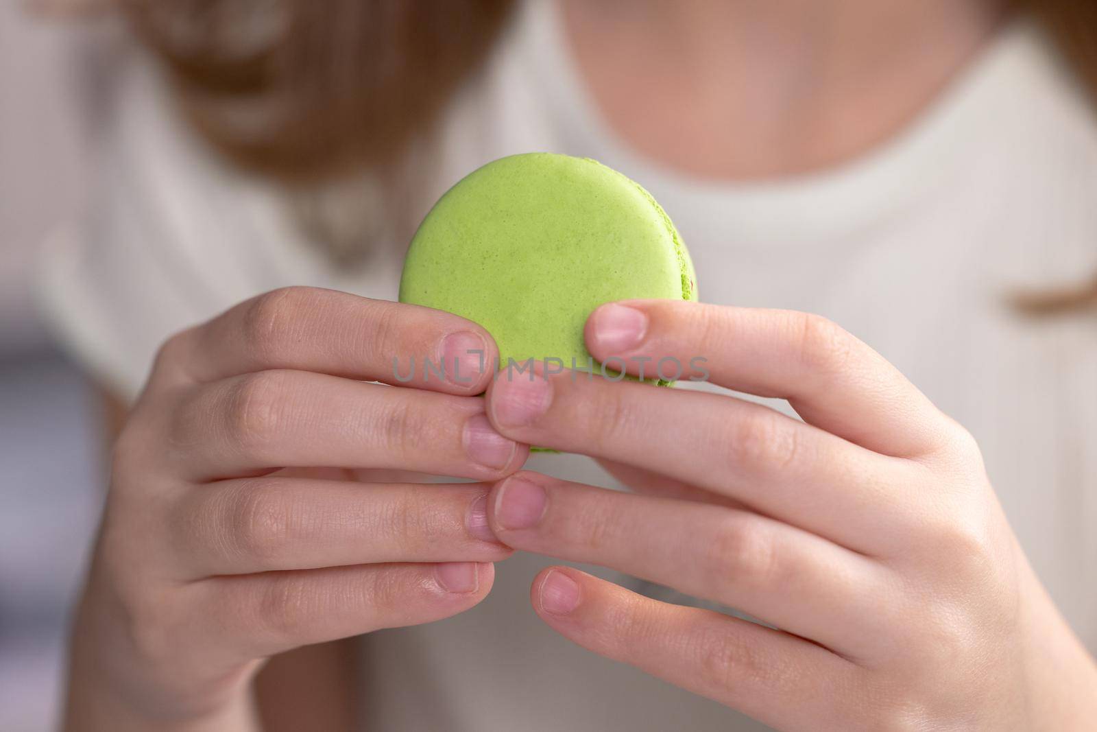 Close up front view, unrecognizable kid brunette girl with big smile and white healthy teeth bites pistachio macaron cookie. Tasty sweet color macaron.