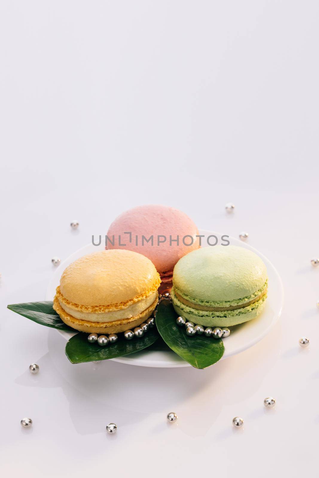 Multicolor macarons , french macaroon, greedy pastry. Macarons on white reflective glass, sweet tasty desserts. French dessert sweets colored macaroons cookies arranged on a while plate.