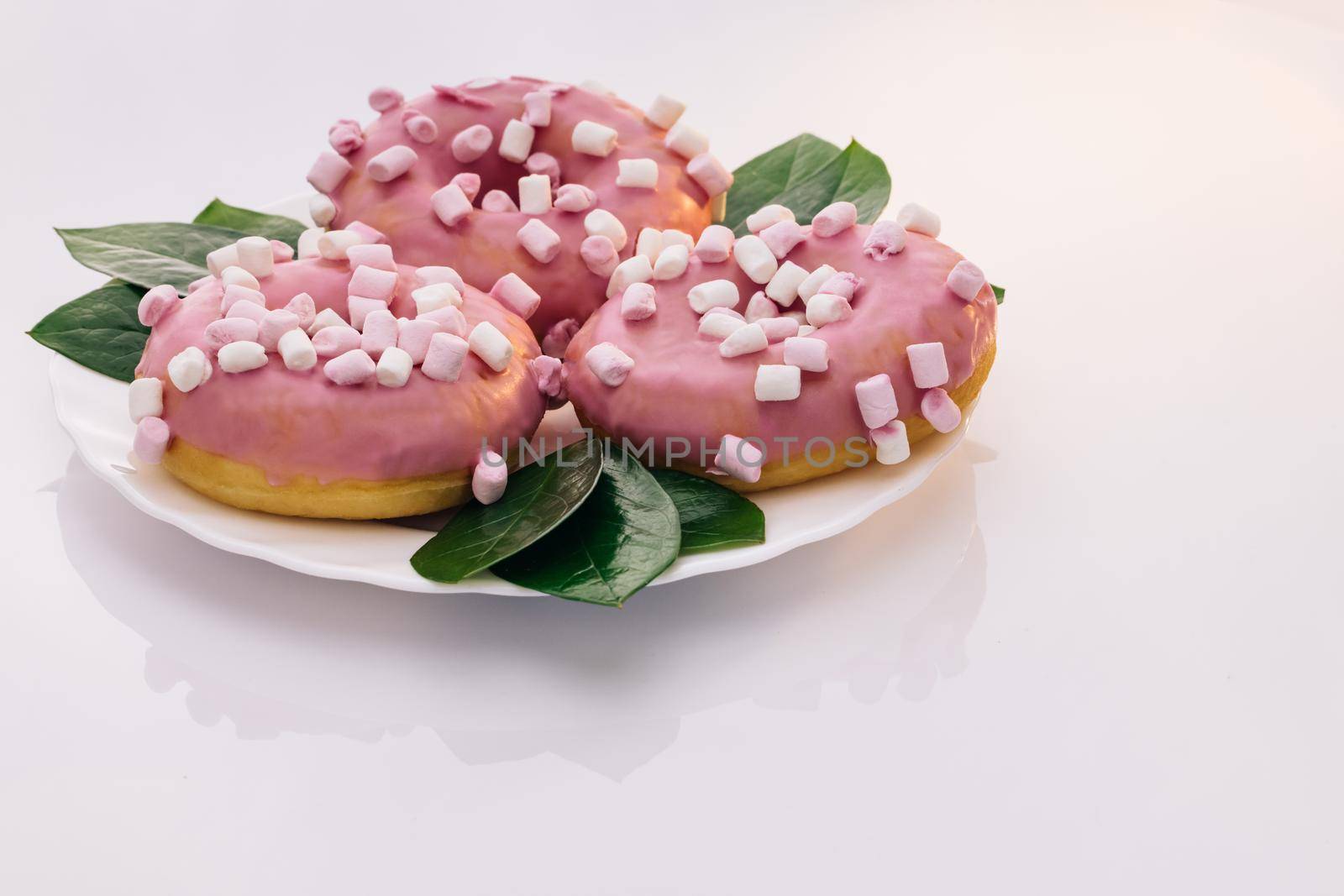Shot of white tasty delicious sweet donut with colorful sprinkles on white background. Colorful frosted pink doughnut. Assorted donuts. Pink glazed and sprinkles donuts. Dessert.