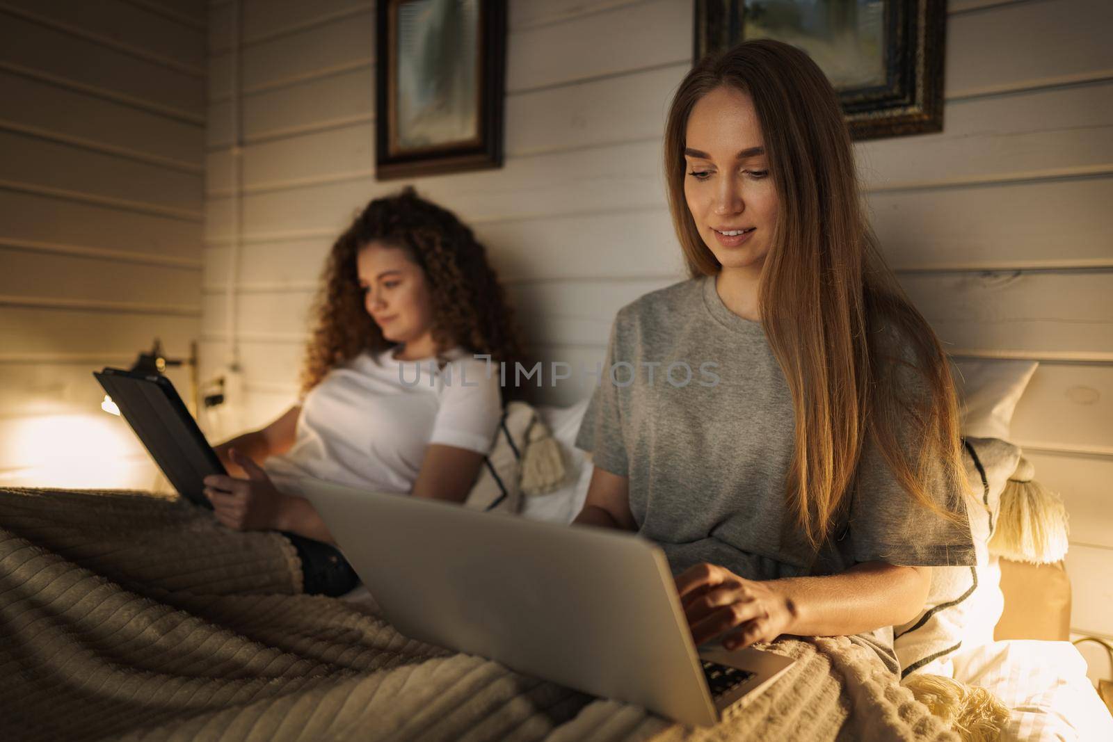 Two beautiful women lying in bed, holding and watching laptop