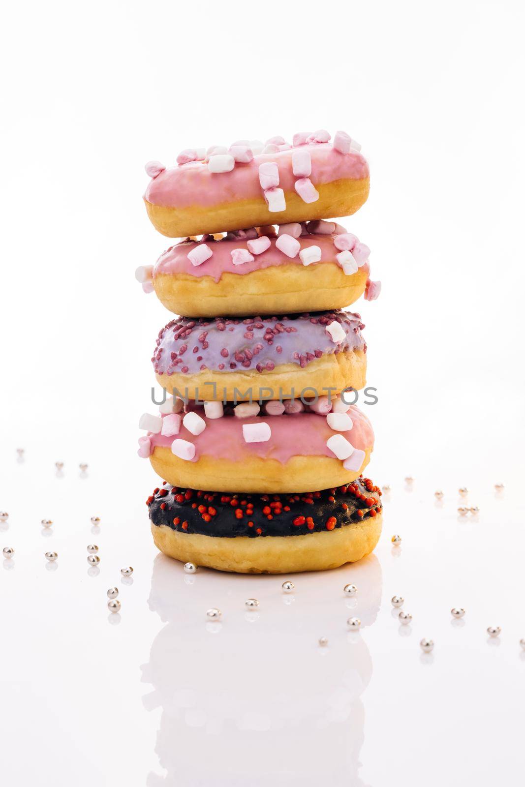 Shot of five sweet doughnuts stacked on top of each other in the form of a tower. Tasty delicious sweet donut with colorful sprinkles on white background. by uflypro