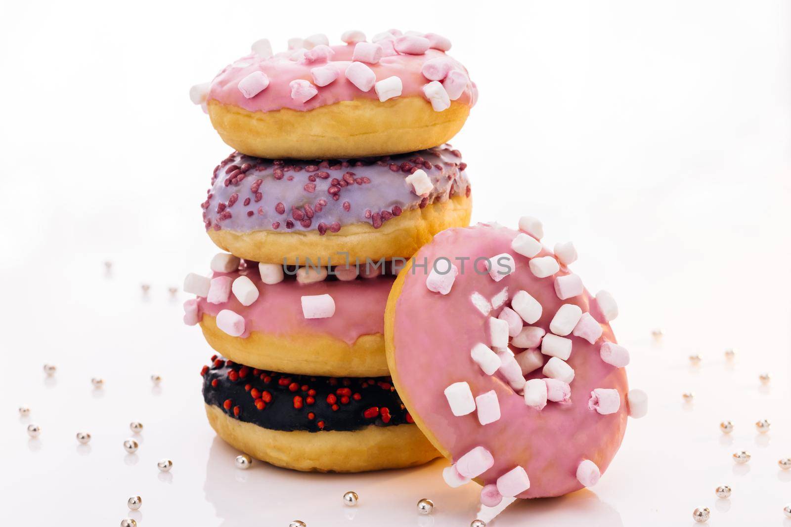 Shot of five sweet doughnuts stacked on top of each other in the form of a tower. Tasty delicious sweet do nut with colorful sprinkles on white background.