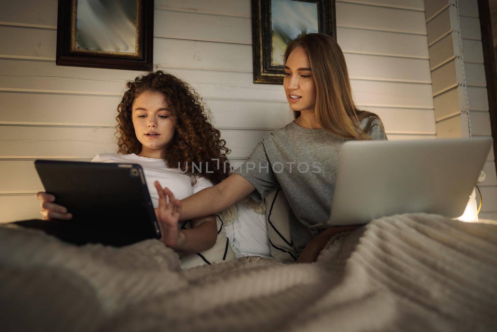 Two beautiful women lying in bed, holding and watching laptop