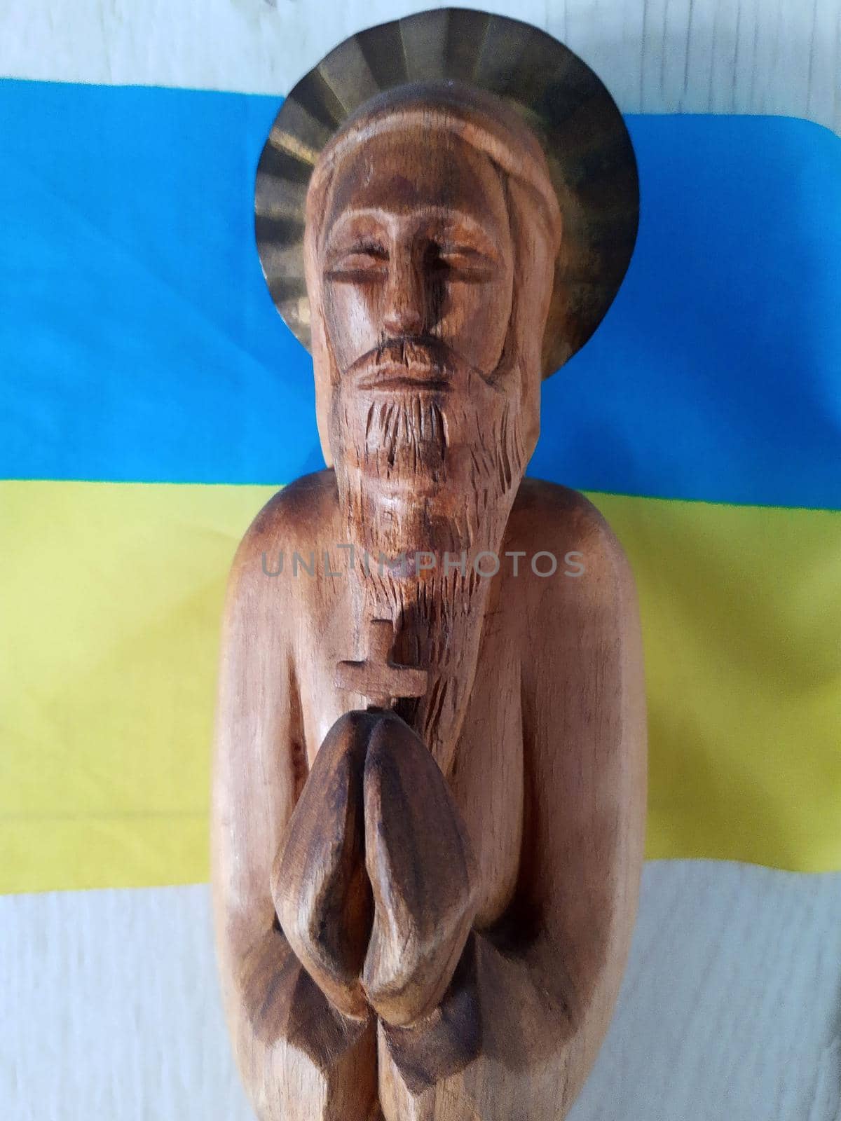 Wooden figurine of the saint against the background of the yellow-blue Ukrainian flag.