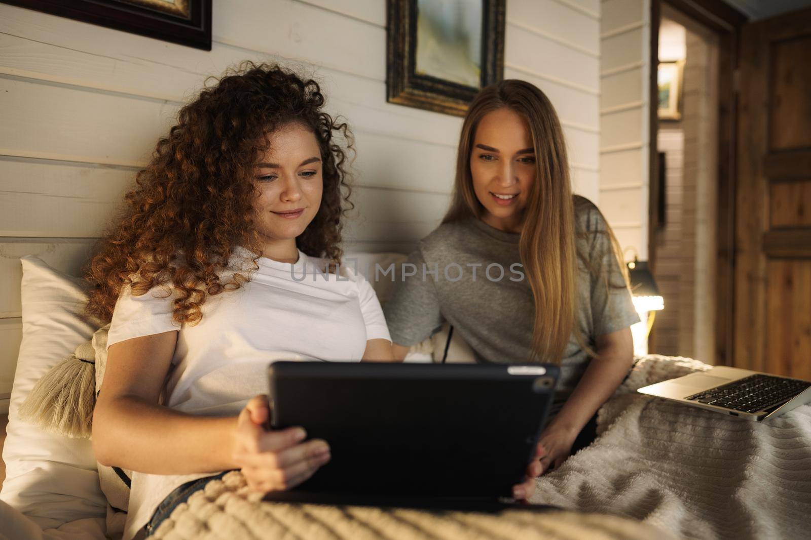 Two beautiful women lying in bed, holding and watching laptop