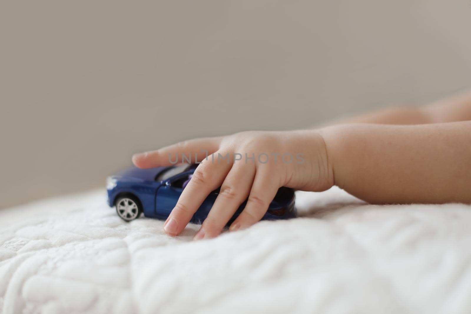 close-up of child hand playing with toy car. hand of a little kid pushing a plastic toy car on the white background.