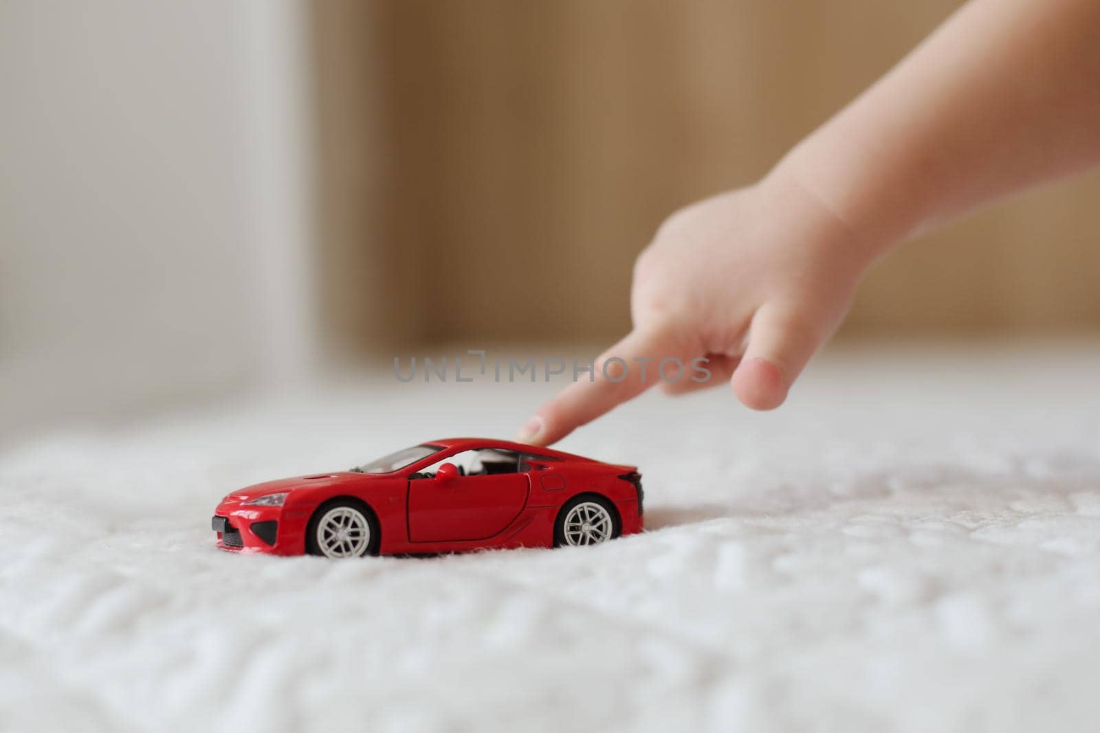 close-up of child hand playing with toy car. hand of a little kid pushing a plastic toy car on the white background.