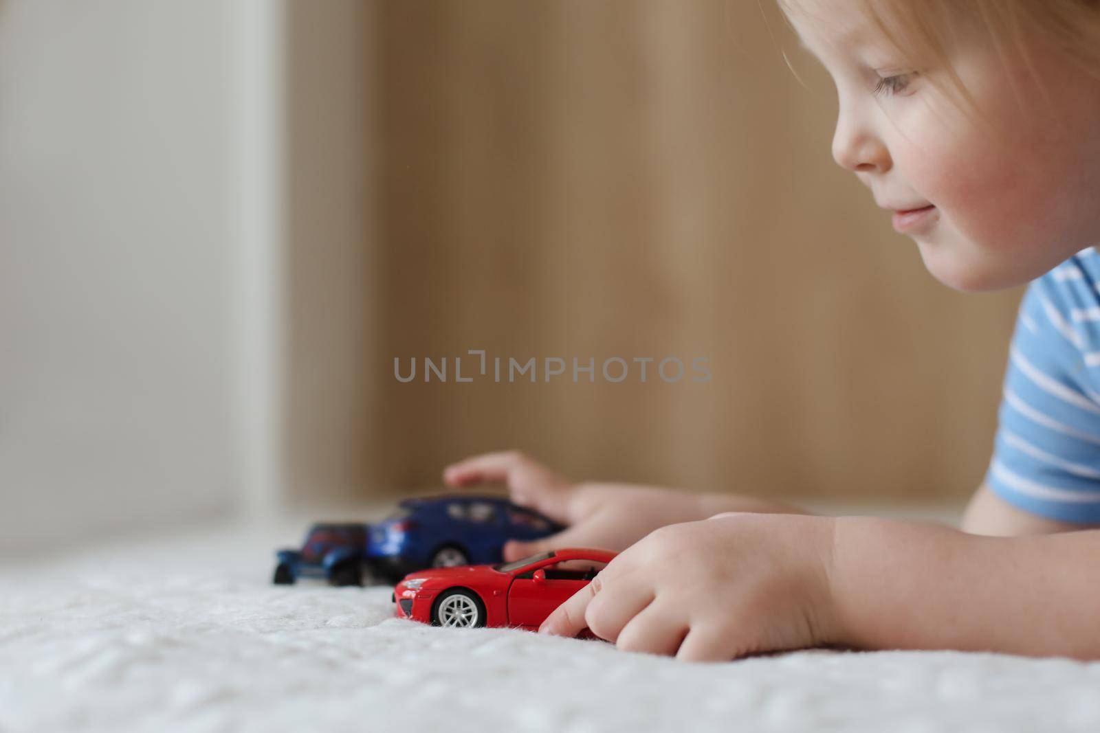 Portrait of child playing with toy cars indoors. Toddler having fun.