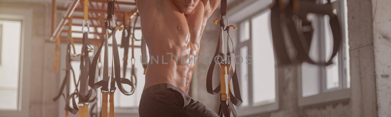 Athletic sporty man in gloves for training holding horizontal bar and performing exercise in the fitness club