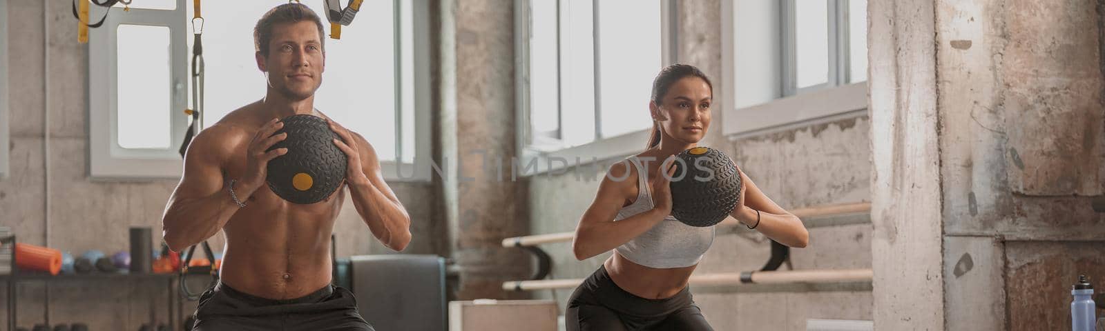 Concentrated sporty man and woman with athletic bodies working out with exercise balls in gym club