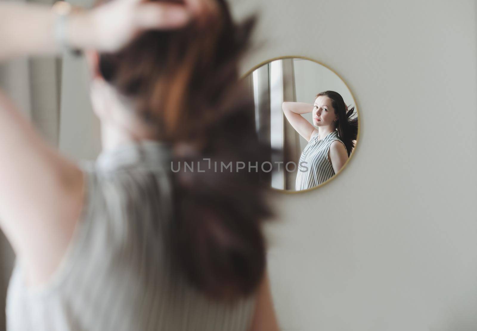 portrait of the young woman looking in the mirror at her hair. 