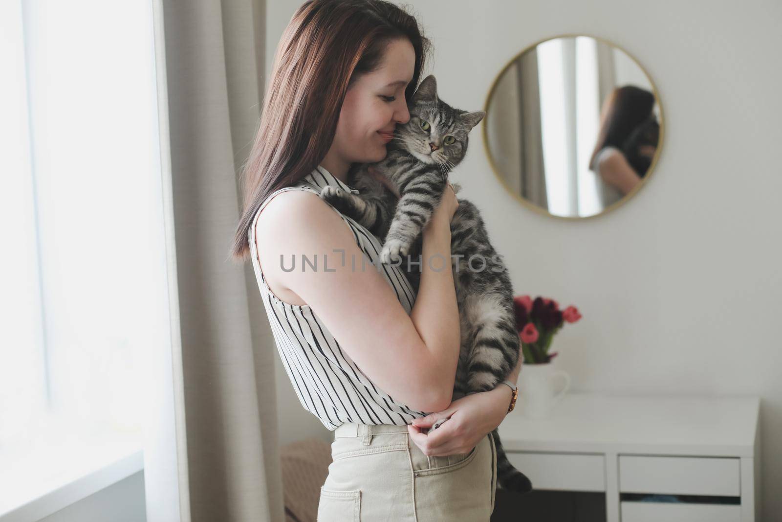A young woman holding a cat at home.