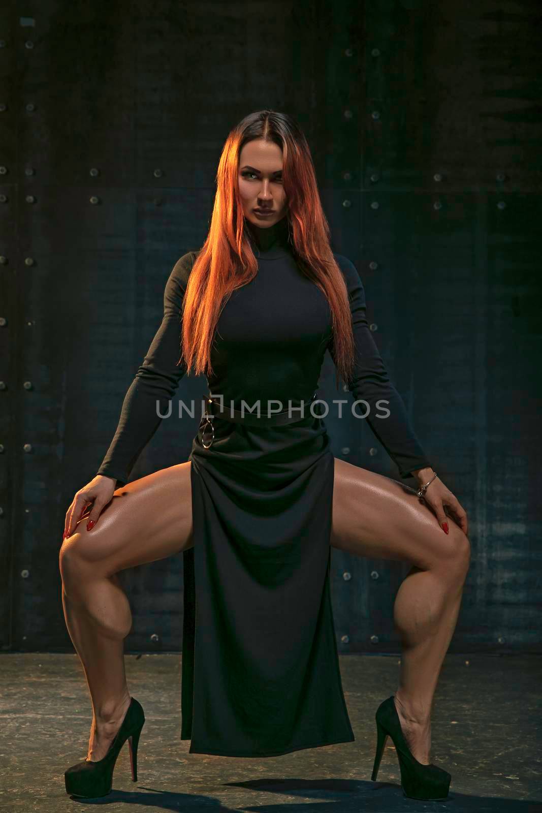 Graceful red-haired girl dances in black dress in the studio in the spotlight on black background