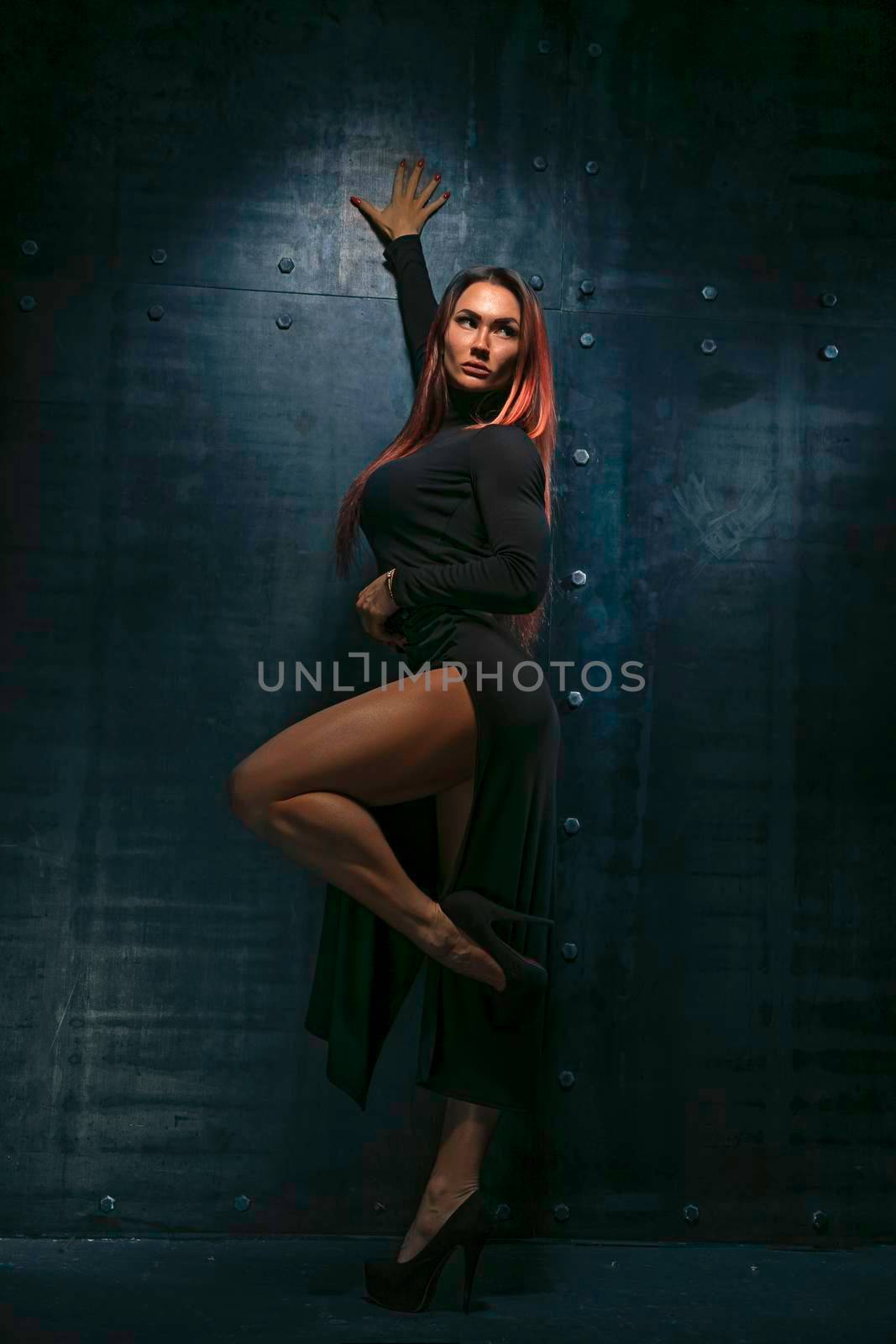 Attractive red-haired girl in black dress with high heels in the studio on metallic background