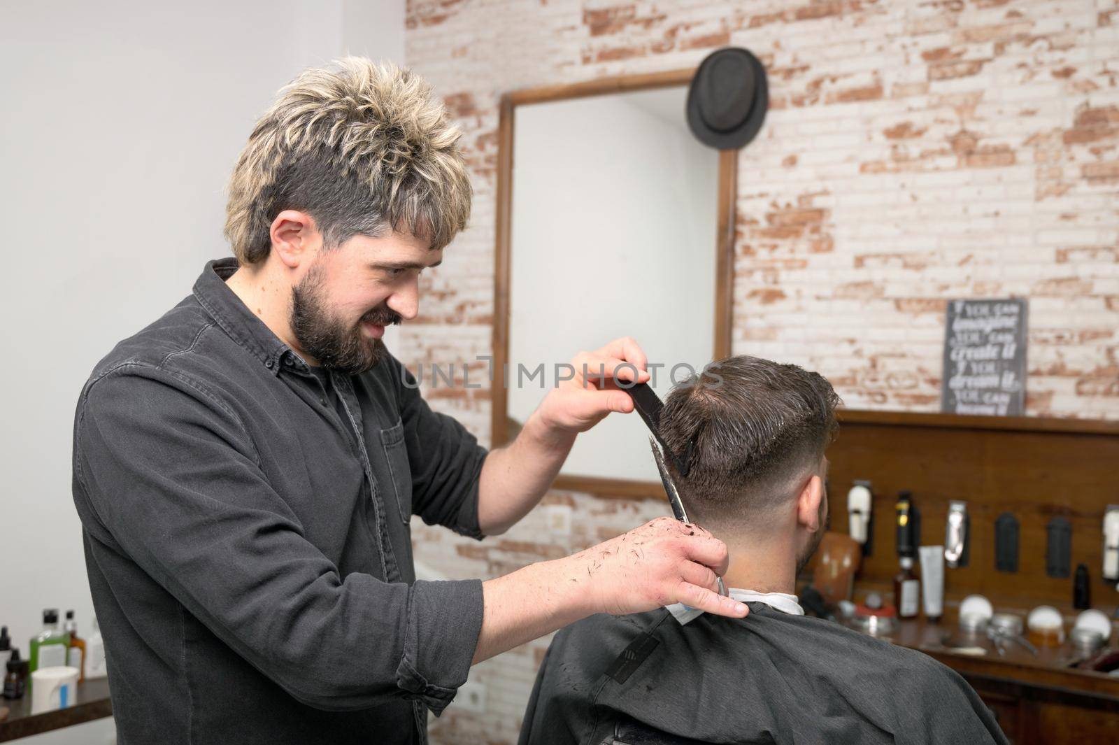 Barber cutting hair with scissors to a handsome young man . High quality photography