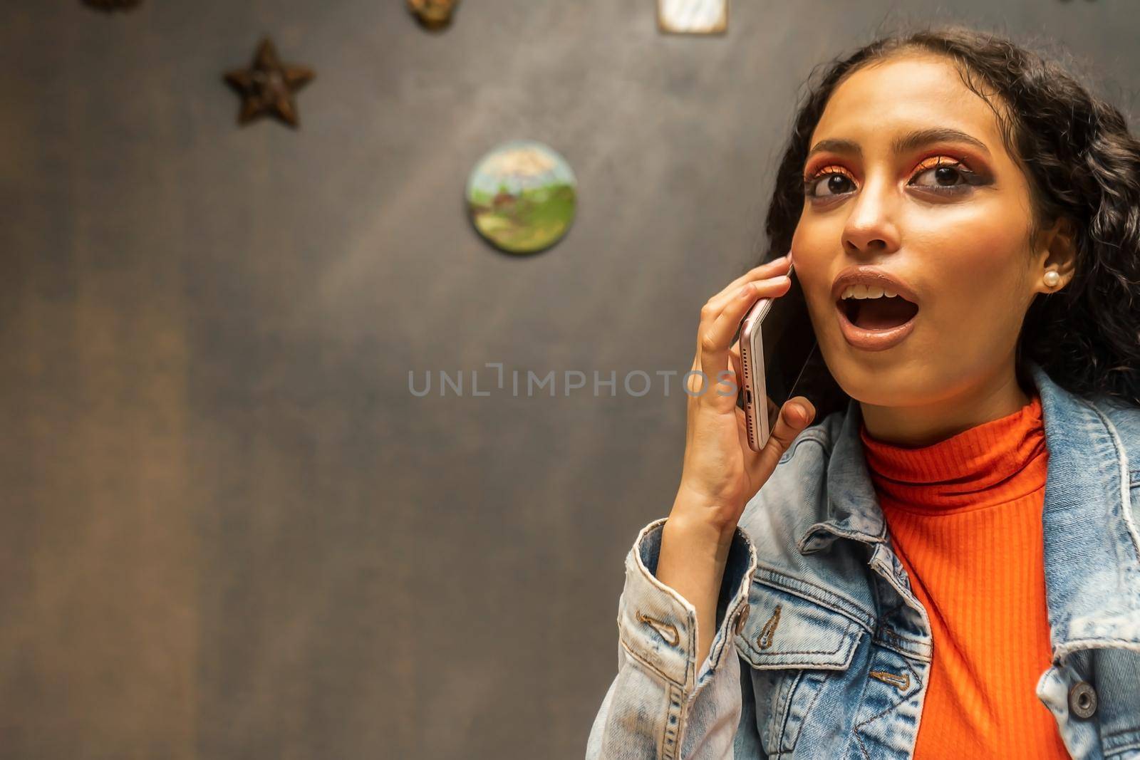 Surprised latin teen talking on cell phone indoors at home.