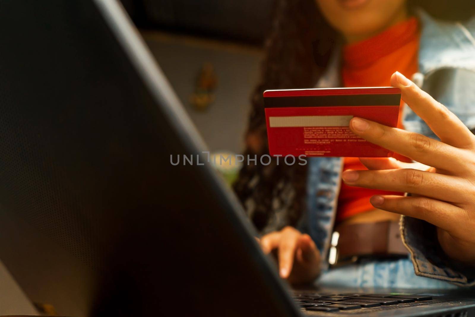 Unrecognizable latin teenager holding his credit card in his hand and making an online purchase by cfalvarez
