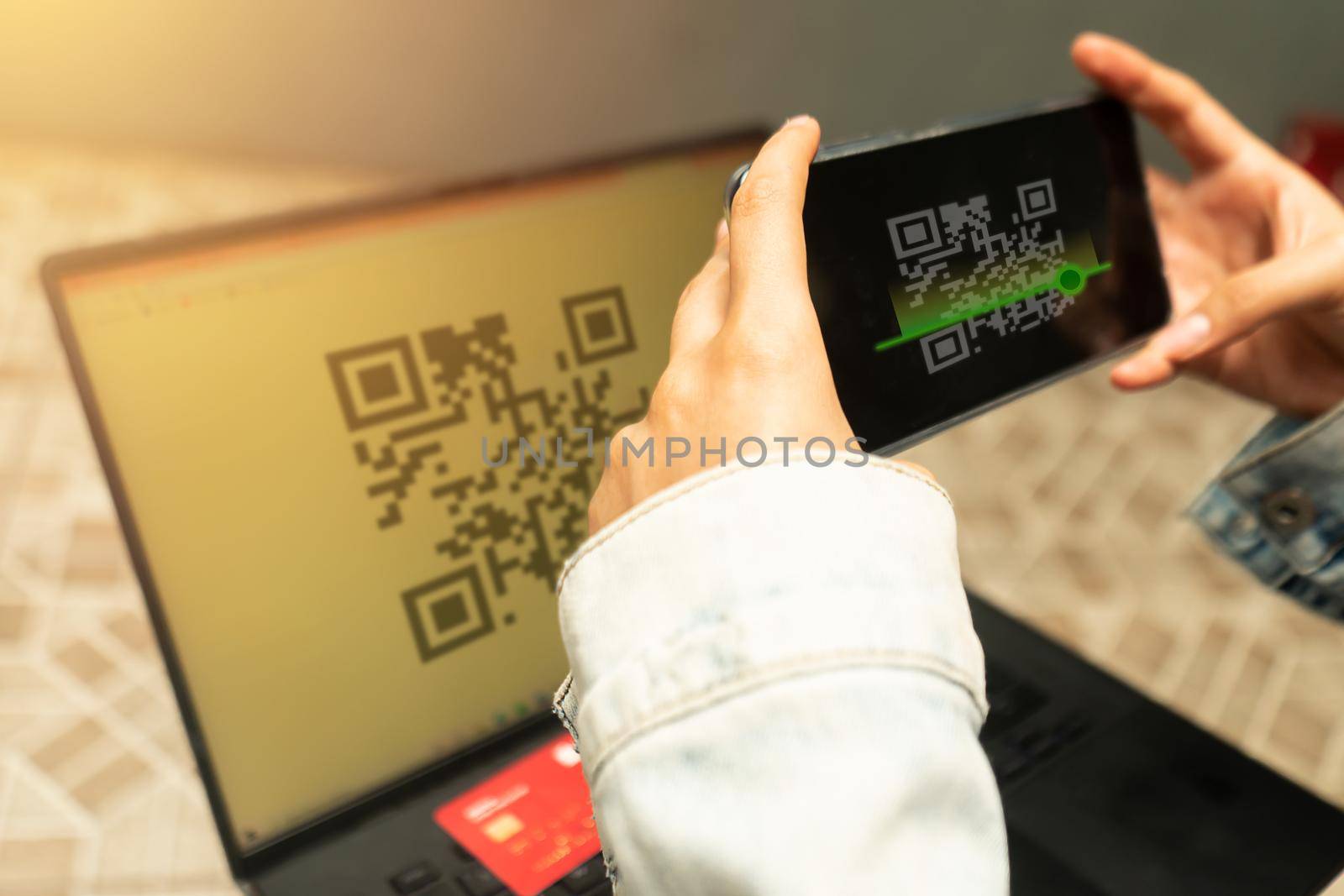Closeup of the hands of a latin teenage girl holding her cell phone and scanning a QR code on her laptop indoors at home.