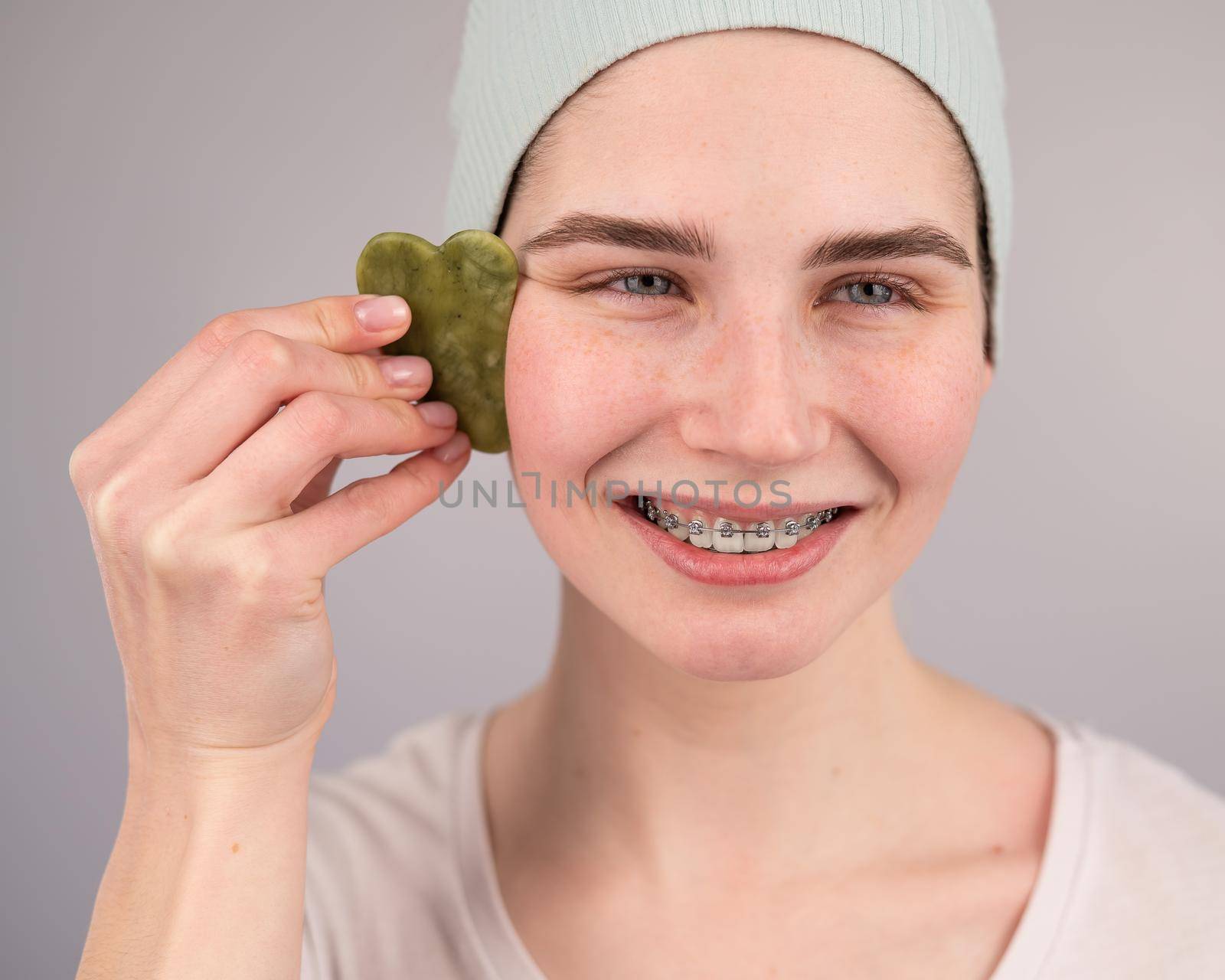 Close-up portrait of a smiling woman with braces doing home care with a gouache massager