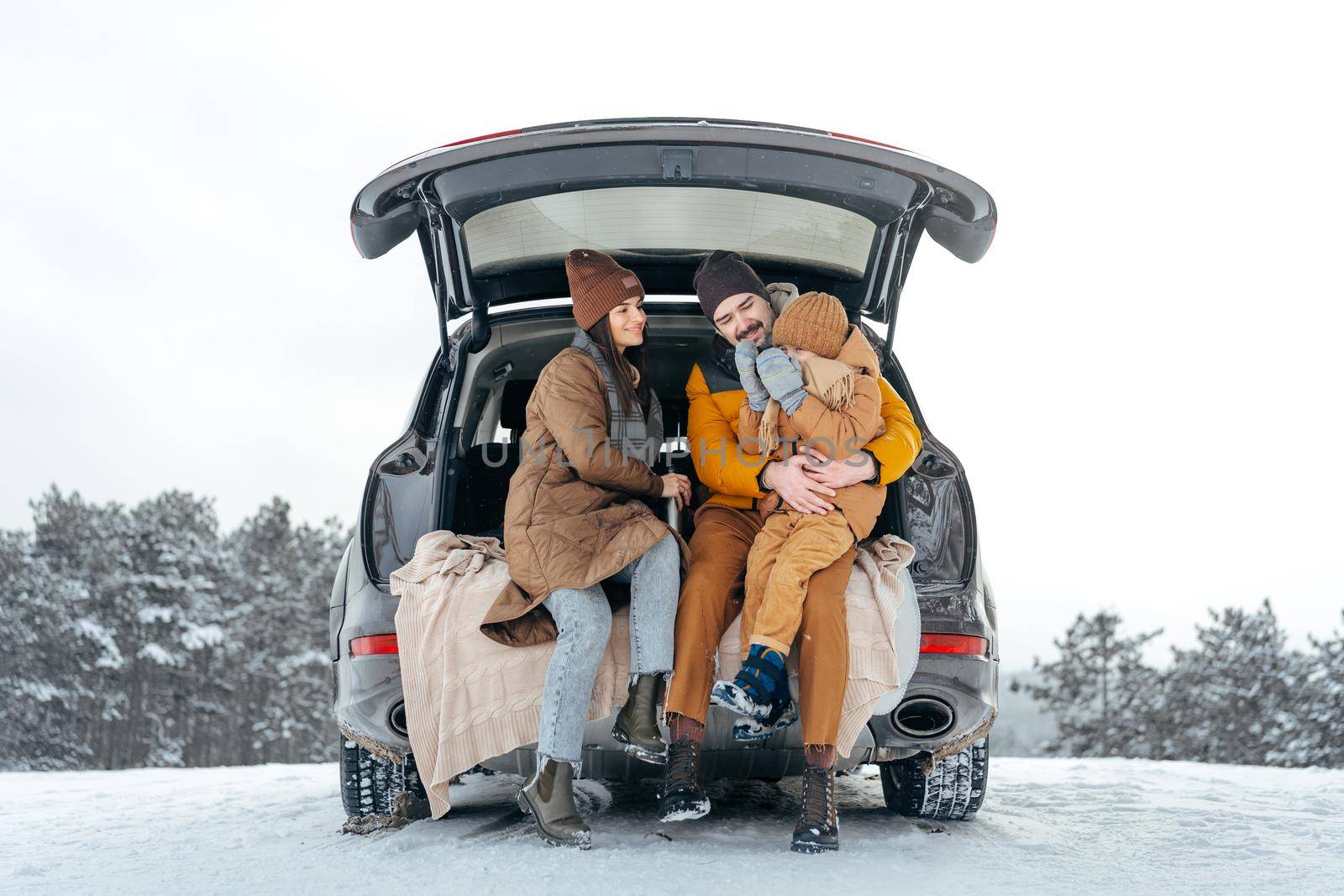 Winter portrait of a family sit on car trunk enjoy their vacation in snowy forest