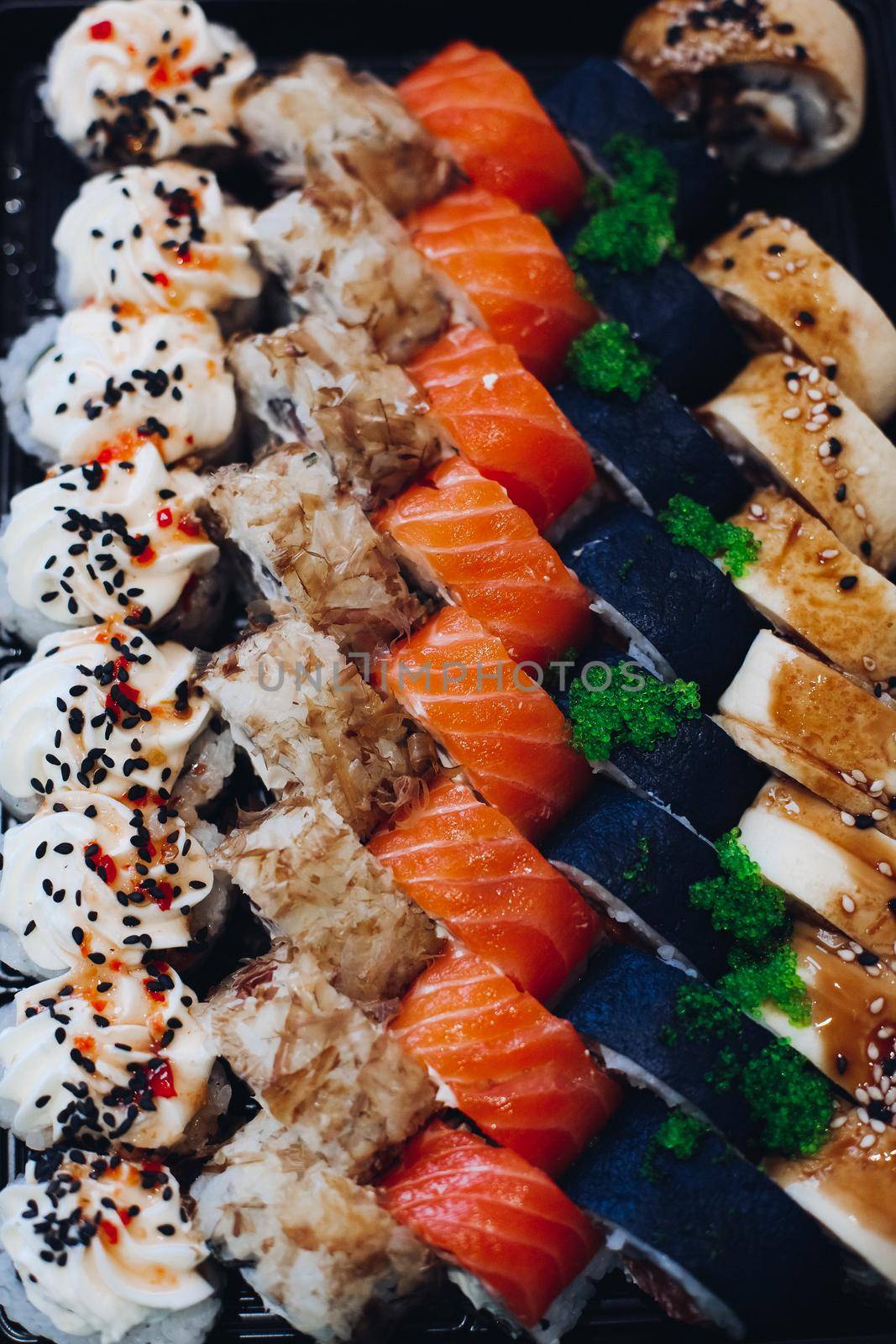 Colorful delicious mouthwatering sushi set laying on the plate including different ingredients: fish, caviar, rice, cucumber, salmon, soy sauce, wasabi, sesame seeds. An interesting presentation.
