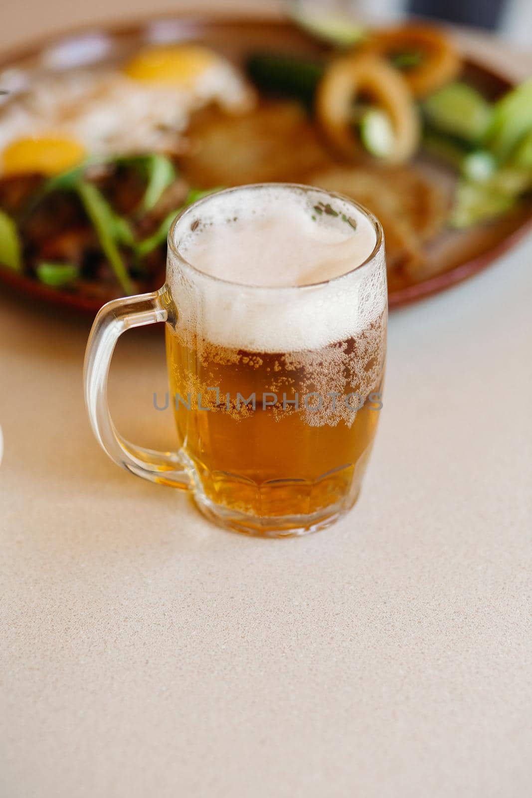 Vertical shot of cold beer cup standing near appetizers plate. by StudioLucky