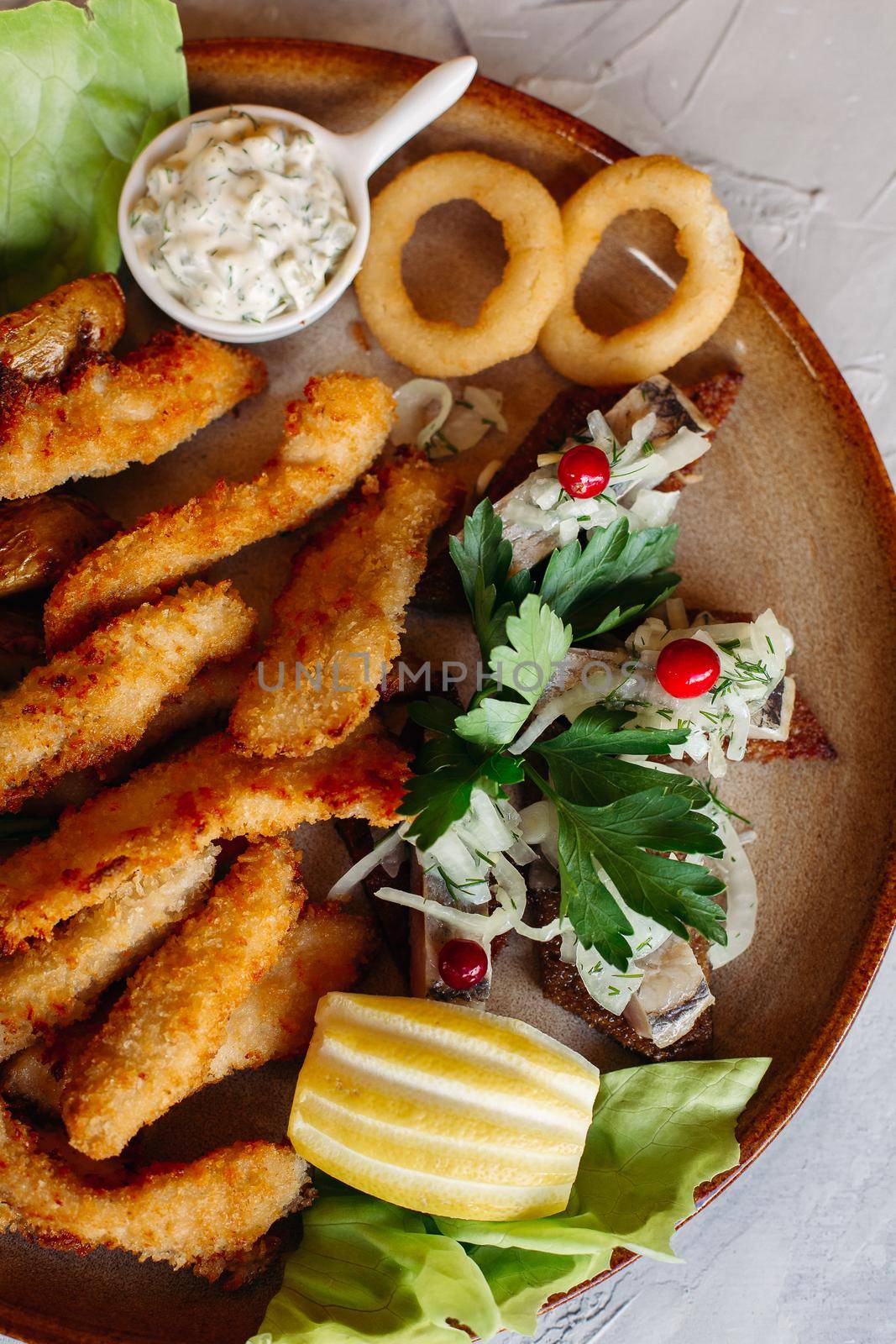 Clay plate full of appetizers served with goldy chicken nuggets cooked with chrispy crust, delicious canapes with herring and cherry tomatoes, garlic sauce, decorated with fresh salad and cheese.