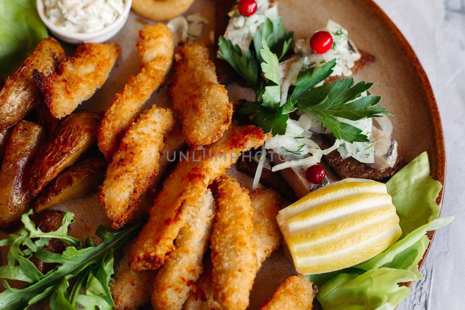 Clay plate full of appetizers served with goldy chicken nuggets cooked with chrispy crust, delicious canapes with herring and cherry tomatoes, garlic sauce, decorated with fresh salad and cheese.