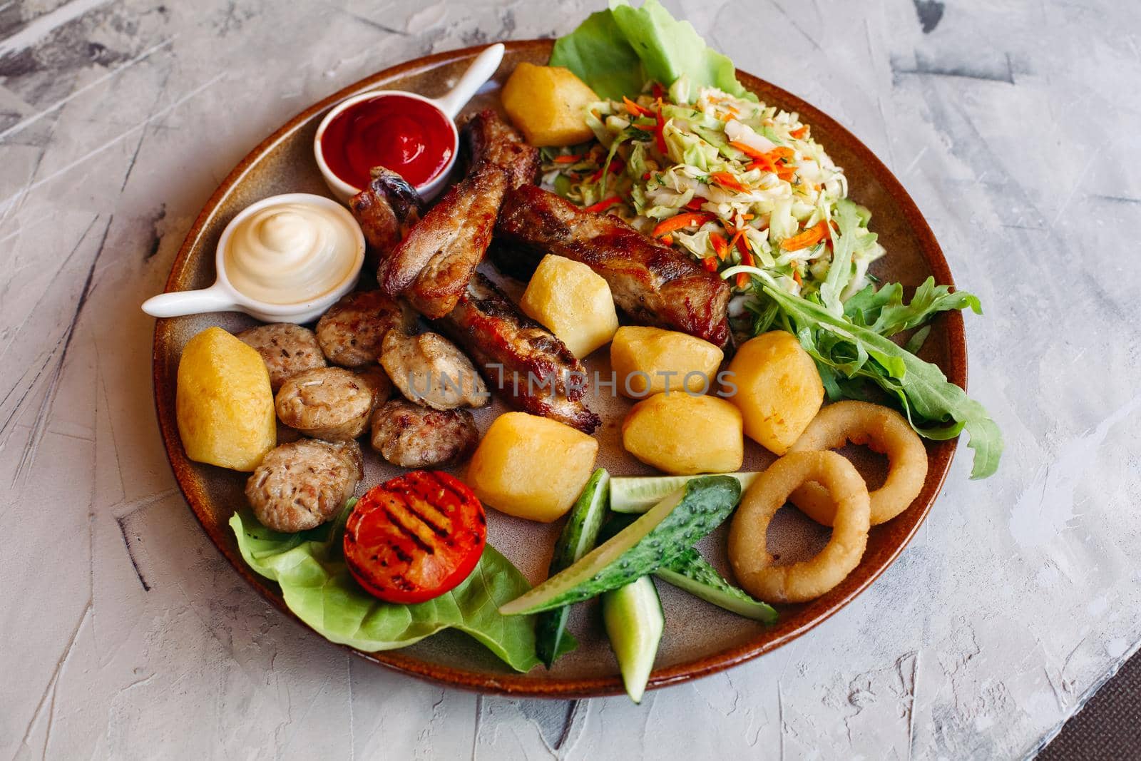 Delicious restaurant appetizers set for beer. vegetable salad, boiled potatoes, grilled chicken legs, roasted onion, sausages, cucmbers, tomatoes and sauces - ketchup and mayo laying on clay plate.